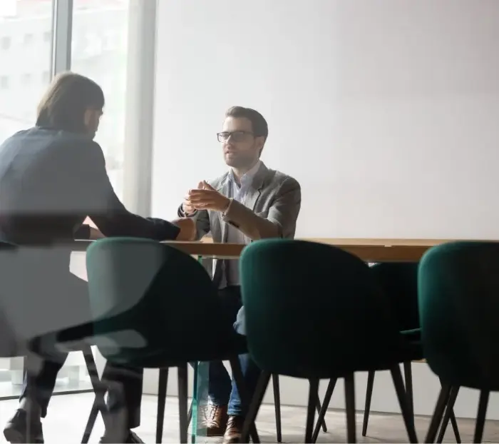 Deux hommes sont assis face à face à une table de bureau et discutent entre eux.