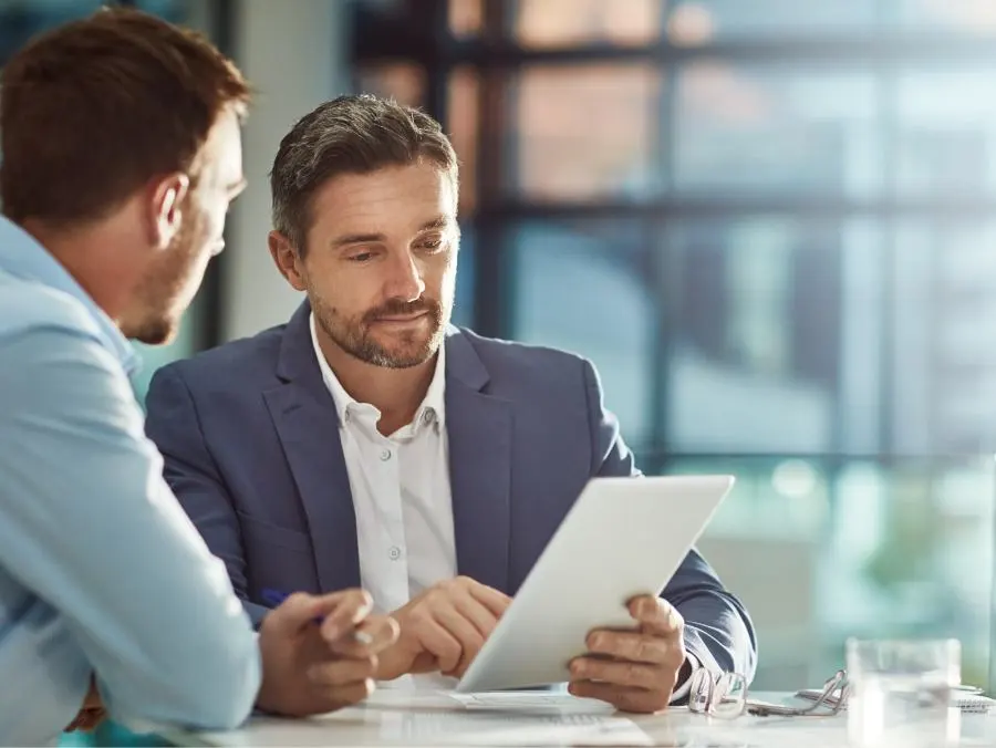 Deux hommes d'affaires sont assis à une table et regardent ensemble une tablette. 