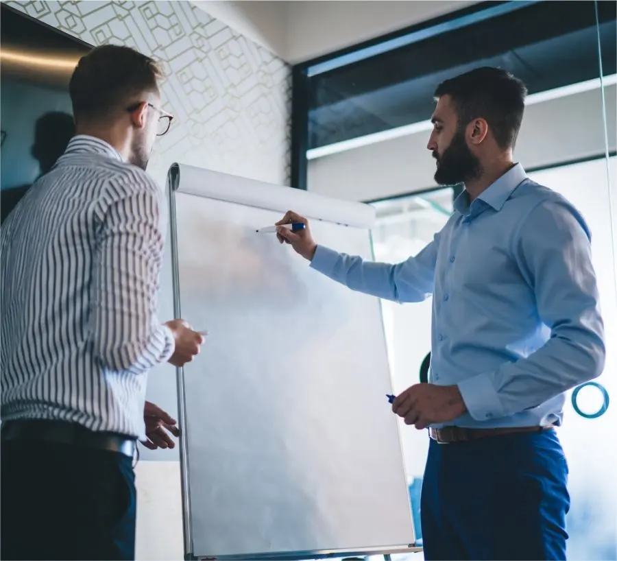 Deux hommes se tiennent devant un tableau blanc et discutent entre eux.