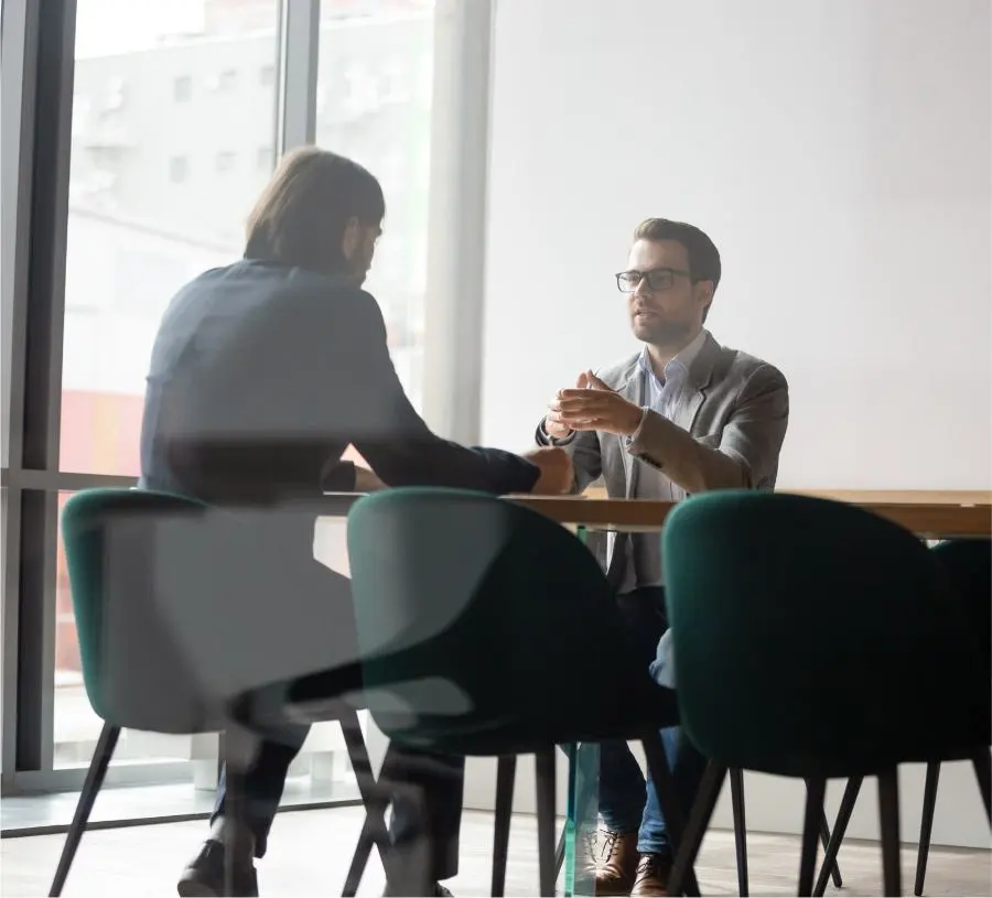 Deux hommes sont assis à une table dans un bureau et discutent.