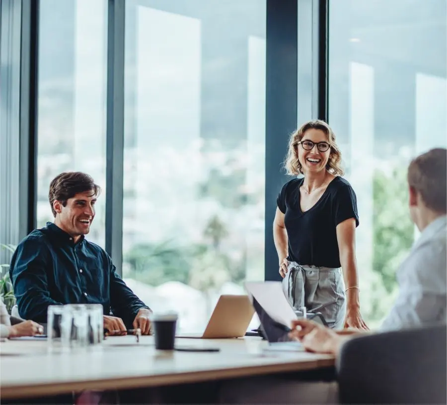 Image d'une femme debout et souriante et d'un homme assis et souriant pendant une réunion au bureau avec vue sur la verdure.