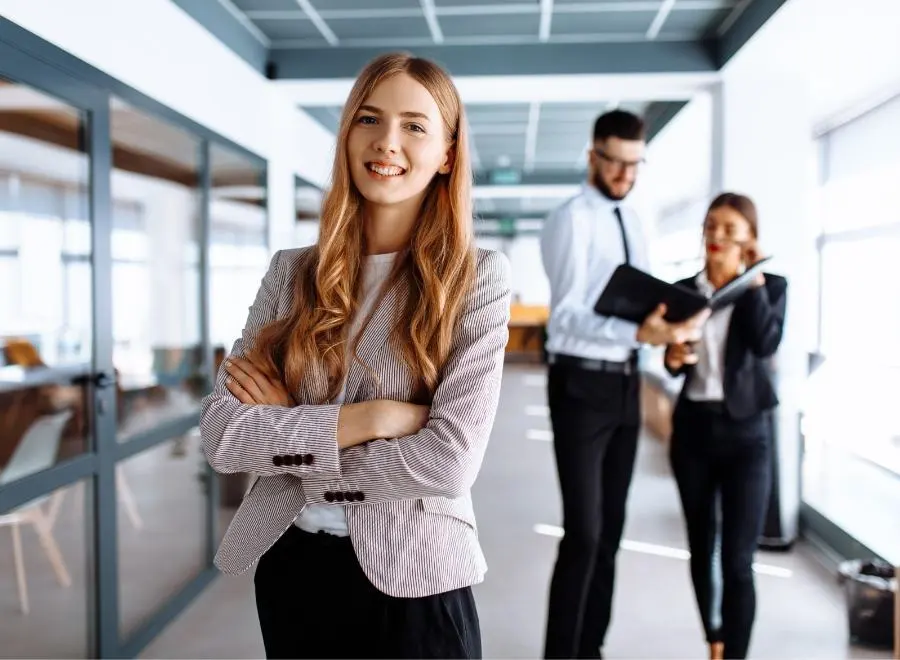 Une jeune femme dans un bureau, les bras croisés, rit avec assurance face à la caméra.