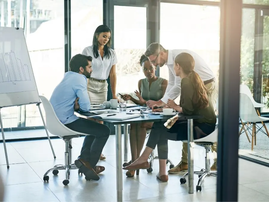 Cinq personnes sont assises autour d'une table dans un bureau et discutent ensemble.