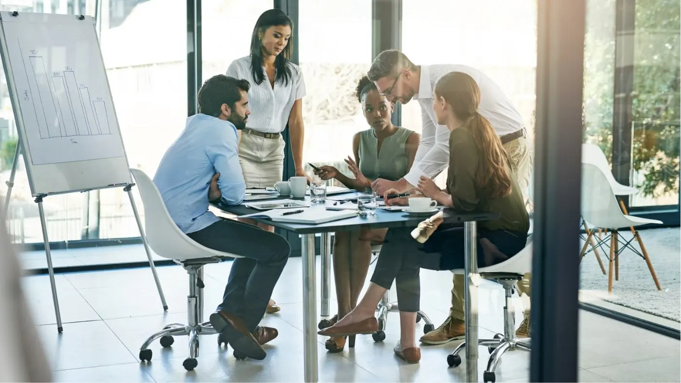 Image de cinq personnes assises à une table de bureau pendant une réunion.