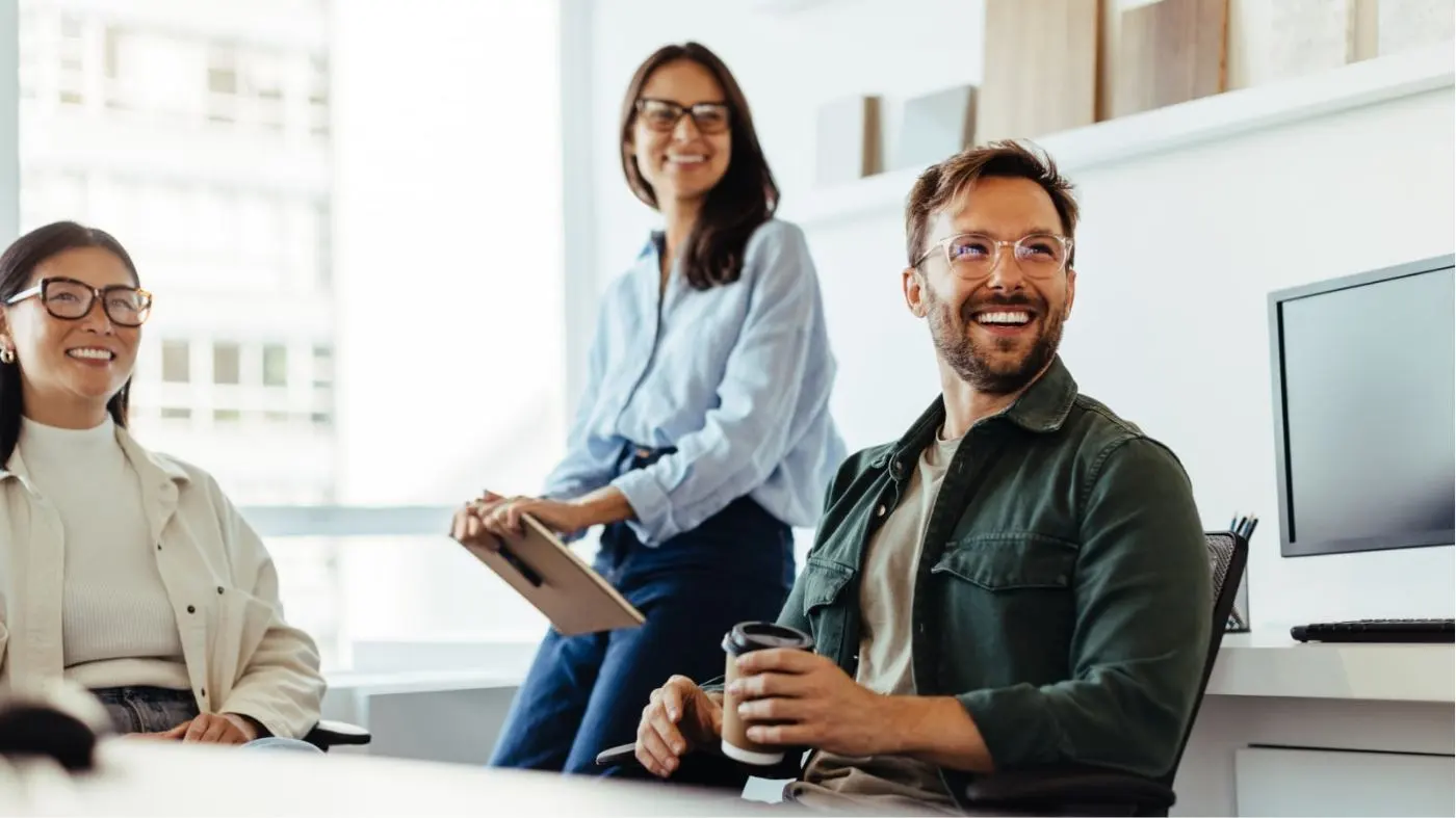 Trois personnes dans un bureau regardent de côté en riant.