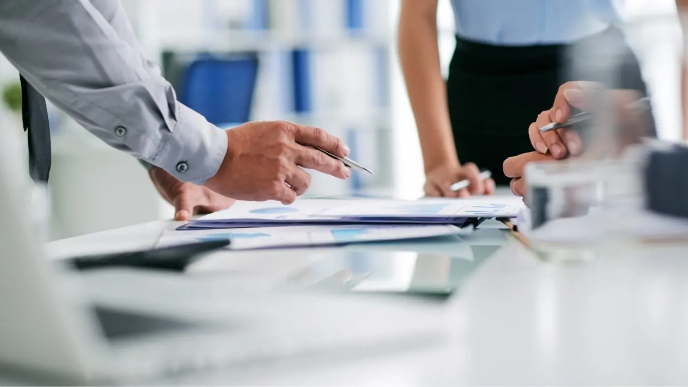 Trois personnes discutent de documents posés devant elles sur la table.